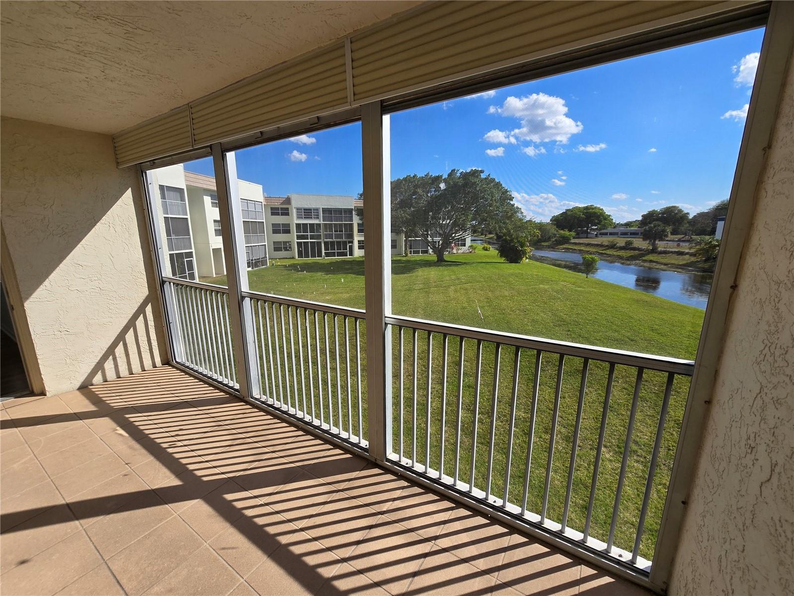 A screened-in balcony overlooks a grassy lawn, a small pond, and neighboring apartment buildings — 6890 Royal Palm Boulevard # 211h, Margate FL 33063, MARGATE, FL