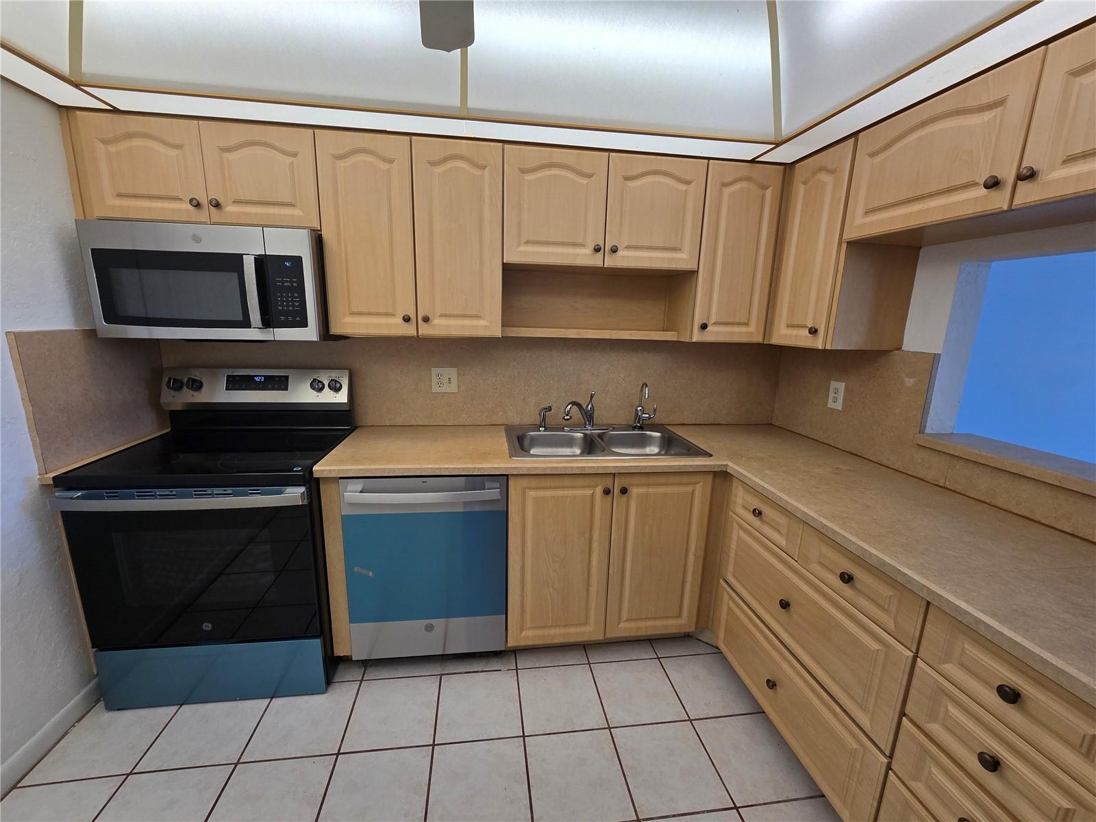A kitchen features light wood cabinets, laminate countertops, stainless steel appliances, and white tiled floors — 6890 Royal Palm Boulevard # 211h, Margate FL 33063, MARGATE, FL