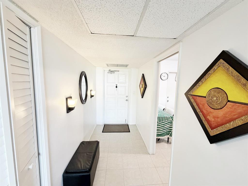 A bright entryway features white walls, tiled flooring, a black bench, and wall art — 2681 S Course Drive # 511, Pompano Beach FL 33069, POMPANO BEACH, FL