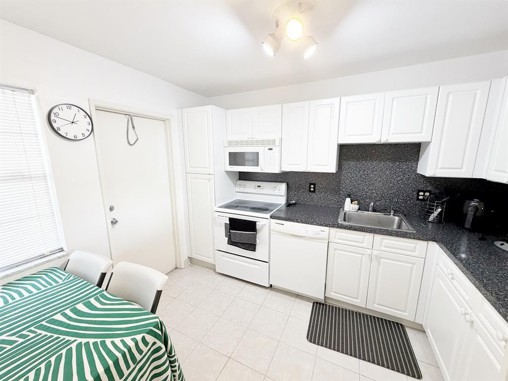 A kitchen features white cabinets, dark countertops, white appliances, and a dining area — 2681 S Course Drive # 511, Pompano Beach FL 33069, POMPANO BEACH, FL