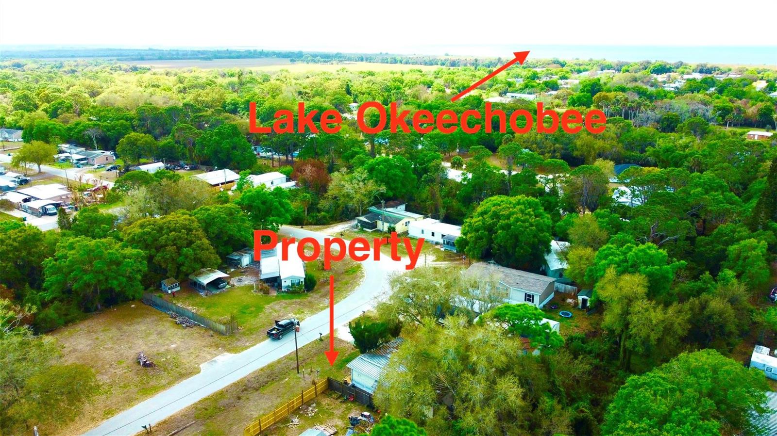An aerial view shows a residential property surrounded by trees with Lake Okeechobee in distance — 6040 SE 91st Trail, Okeechobee FL 34974, OKEECHOBEE, FL