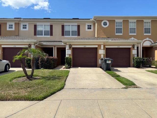 A row of multi-story townhomes features beige stucco exteriors, brown garage doors, and concrete driveways — 222 BEXLEY DRIVE, DAVENPORT, FL