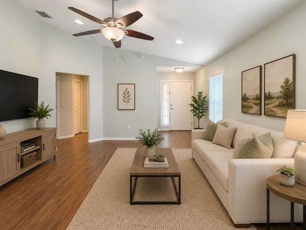 A living room features a vaulted ceiling, wood-look flooring, a sofa, and a television console — 7115 FOREST MERE DRIVE, RIVERVIEW, FL