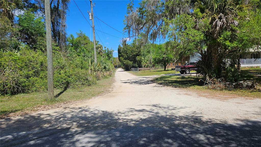 A dirt road leads past a utility pole and trees toward a parked red truck — 11201 W GEM STREET, CRYSTAL RIVER, FL