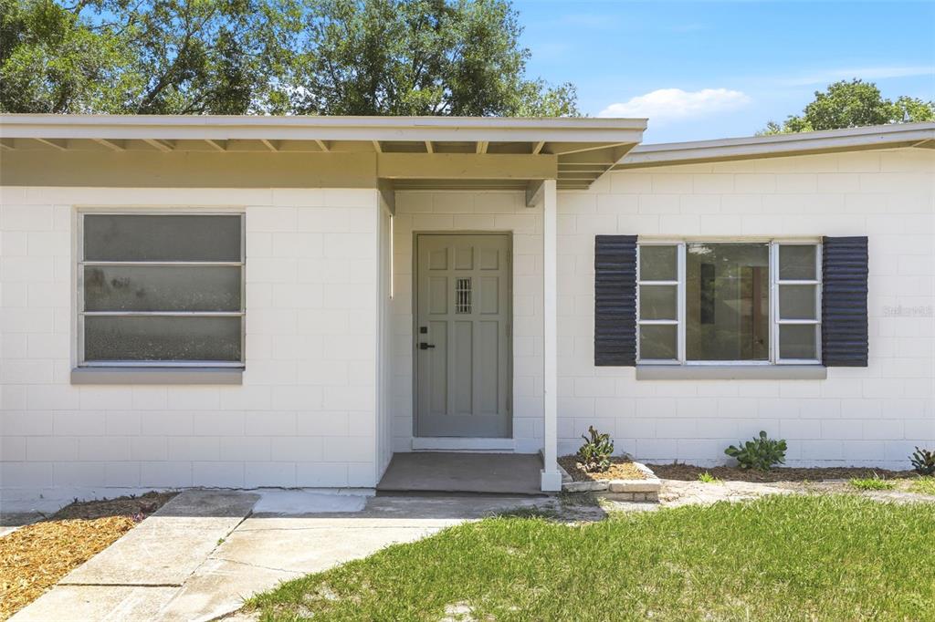 A white concrete block house exterior features a gray front door and two windows — 1300 MORNINGSIDE STREET, MOUNT DORA, FL