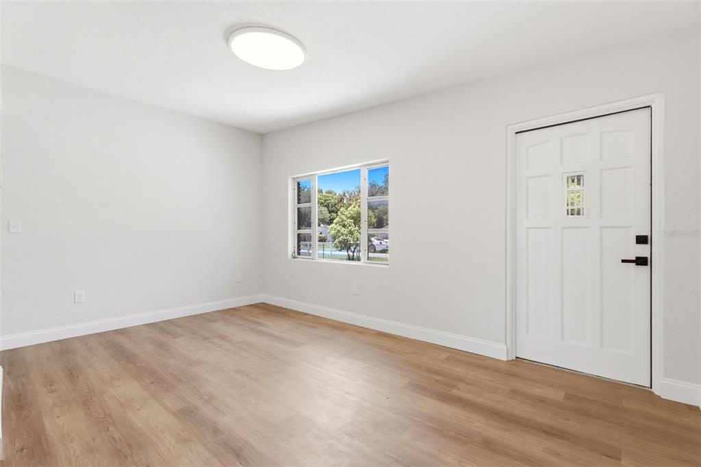 A bright, empty room features light wood-look flooring, white walls, a window, and a door — 1300 MORNINGSIDE STREET, MOUNT DORA, FL