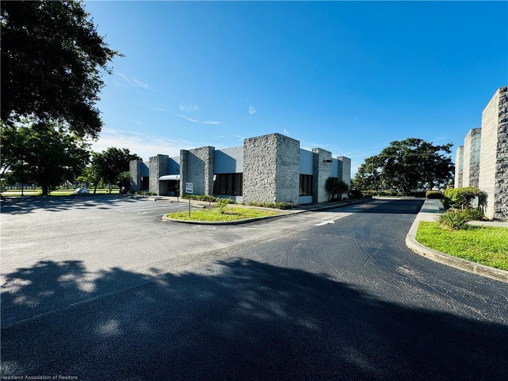A single-story commercial building with stone-textured exterior walls and a large asphalt parking lot — 346 E ROYAL PALM STREET, LAKE PLACID, FL