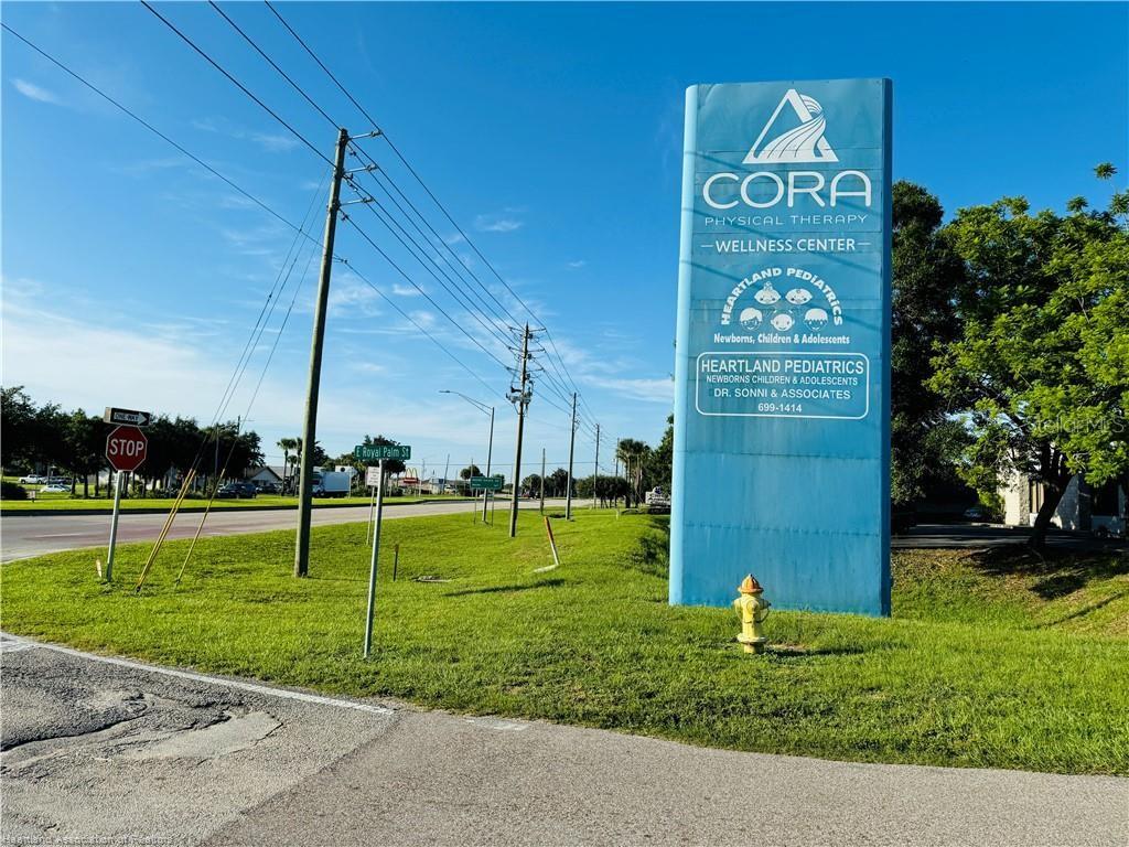 A blue sign for CORA Physical Therapy and Heartland Pediatrics stands on a grassy lawn — 346 E ROYAL PALM STREET, LAKE PLACID, FL