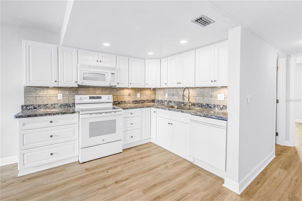 A kitchen with white cabinets, granite countertops, stainless steel appliances, and light wood-look flooring — 7625 SUN ISLAND DRIVE S UNIT 106, SOUTH PASADENA, FL