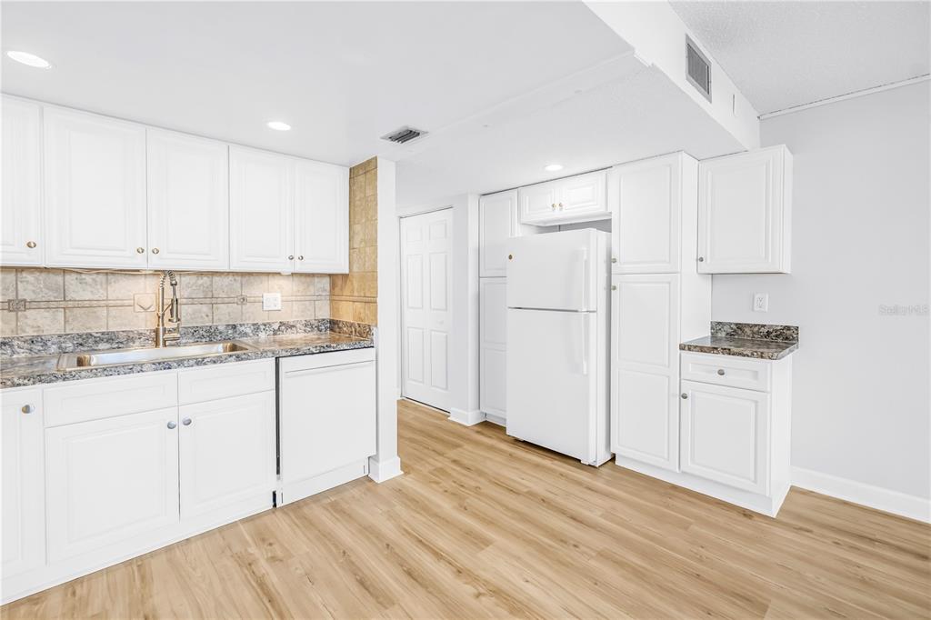 A kitchen with white cabinets, granite countertops, a white refrigerator, and light wood-look flooring — 7625 SUN ISLAND DRIVE S UNIT 106, SOUTH PASADENA, FL