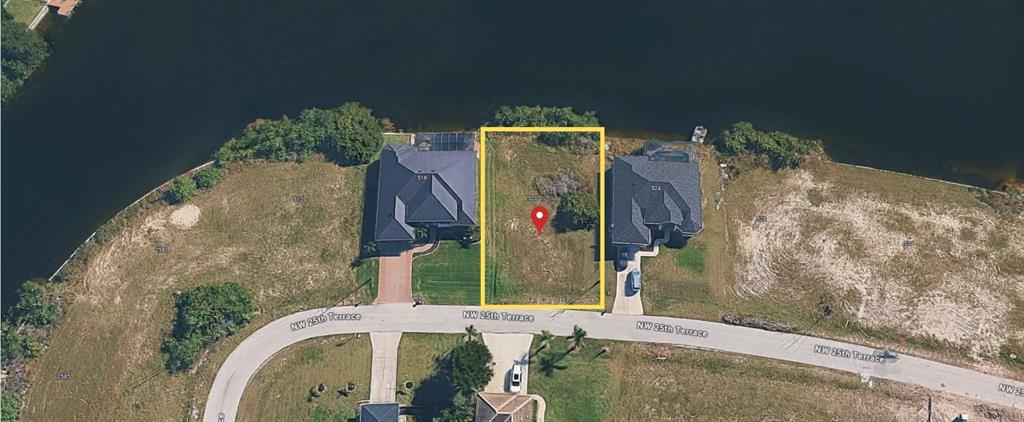 An aerial view shows a vacant waterfront residential lot outlined in yellow between two houses — 520 NW 25TH TERRACE, CAPE CORAL, FL