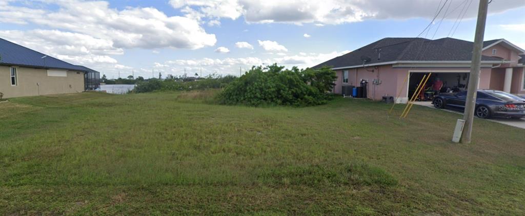 A vacant grassy lot sits between two suburban houses with a view of water behind — 520 NW 25TH TERRACE, CAPE CORAL, FL