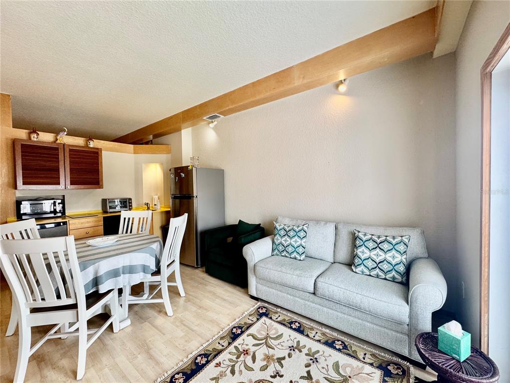 A living and dining area features a light gray sofa, wooden beam, and kitchen appliances — 101 PALM HARBOR PARKWAY UNIT A305, PALM COAST, FL