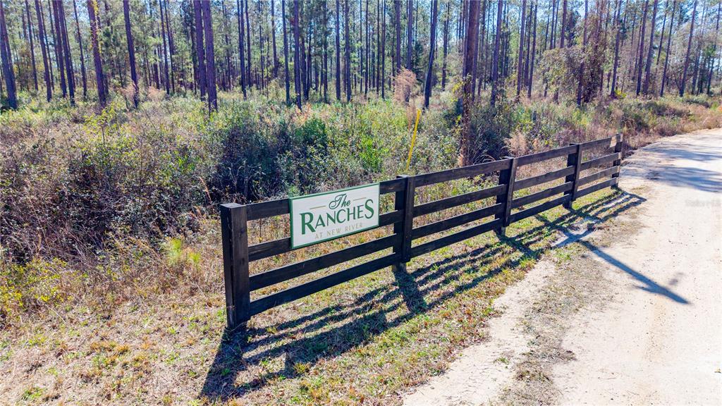 A wooden fence with a sign reading The Ranches at New River borders a dirt road — TBD NW CR 235, LAKE BUTLER, FL