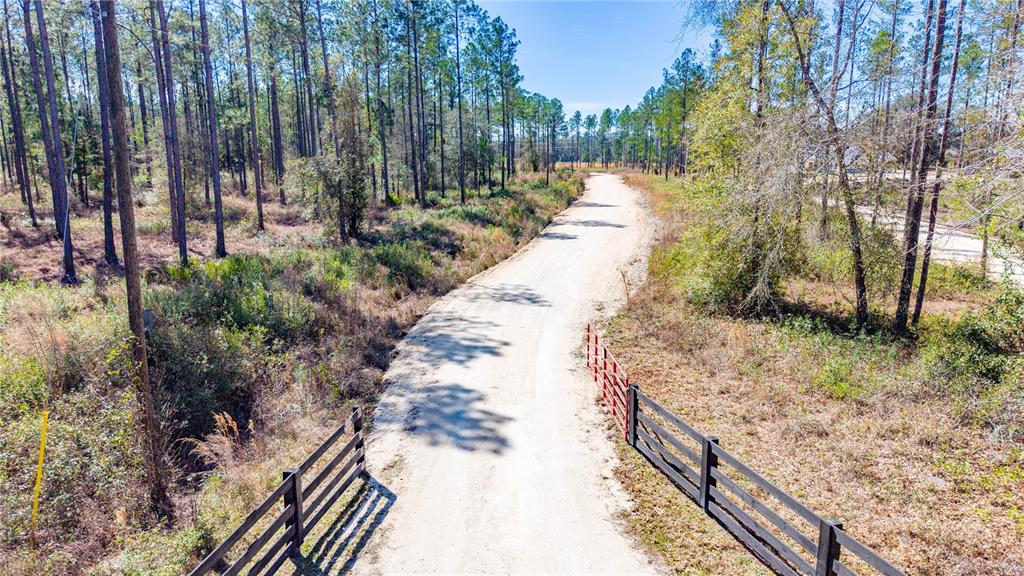 An aerial view shows a dirt road leading through a wooded area with wooden fencing — TBD NW CR 235, LAKE BUTLER, FL