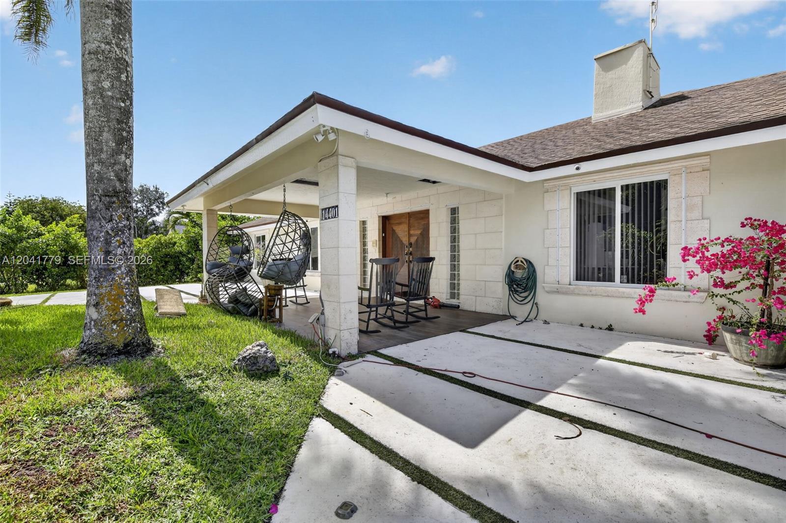 A house exterior features a covered porch with hanging chairs, rocking chairs, and a driveway — DAVIE, FL