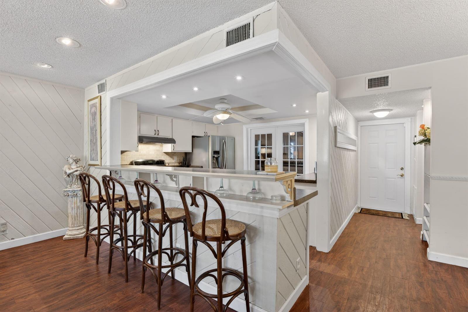A kitchen with a breakfast bar, four wooden stools, and wood-look flooring — 3951 NE 17th Avenue # 703, Pompano Beach FL 33064, POMPANO BEACH, FL