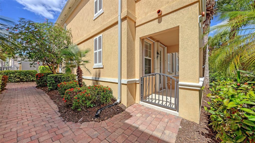 A paved walkway leads to a gated entryway of a yellow stucco building with landscaping — 1586 DORGALI DRIVE, SARASOTA, FL