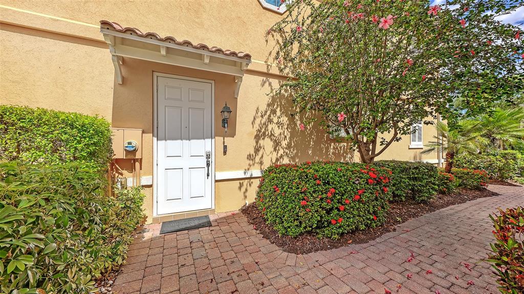 A white front door with a small awning sits beside a brick walkway and landscaping — 1586 DORGALI DRIVE, SARASOTA, FL