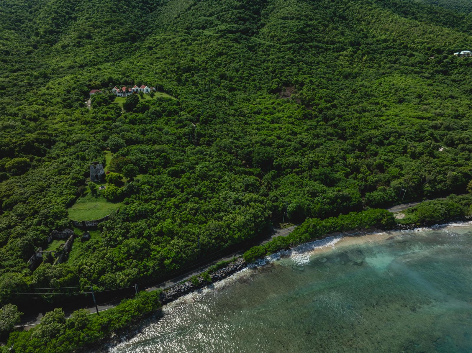 An aerial view shows a coastal road, a historic stone tower, and hillside residential buildings — 104 N Cane Bay Estate N, FL