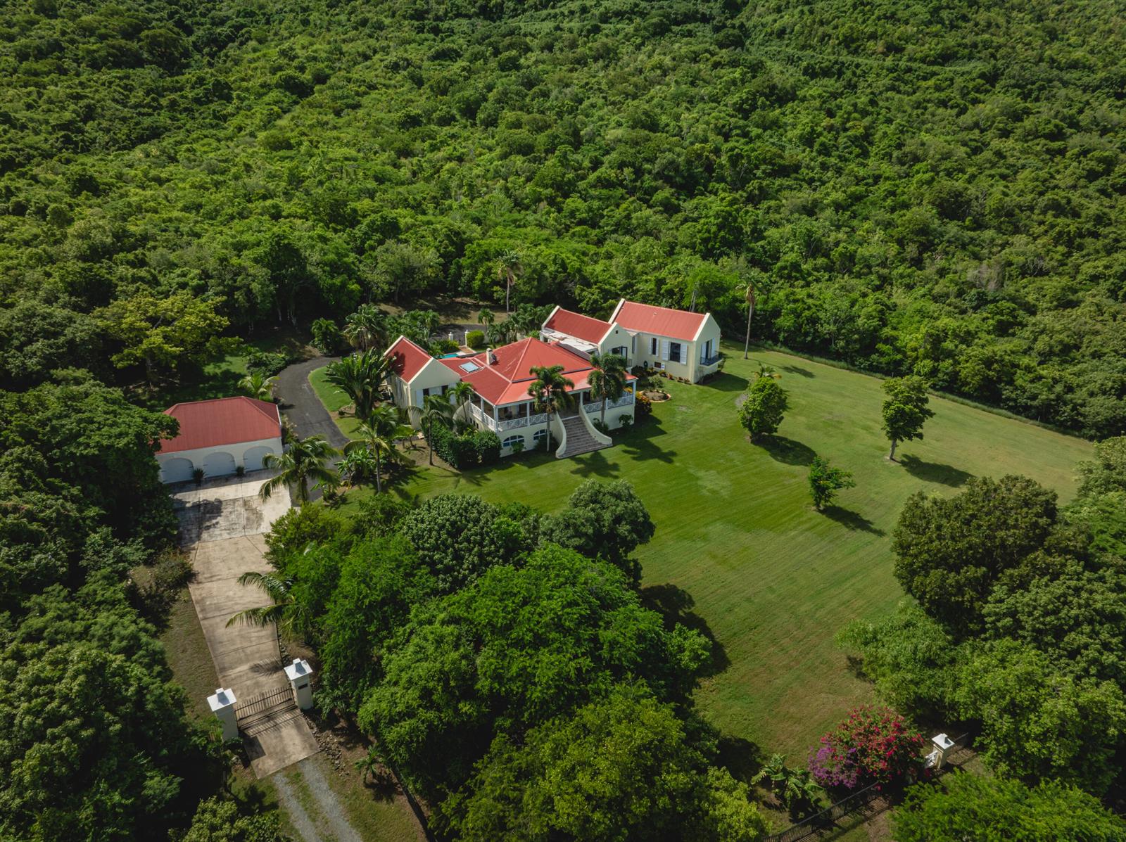 An aerial view of a yellow house with a red roof surrounded by green forest — 104 N Cane Bay Estate N, FL
