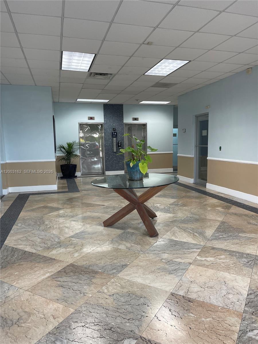 This office building lobby features a glass-topped table, marble tile flooring, and two elevators — 717 Ponce De Leon Blvd # 323, Coral Gables FL 33134, CORAL GABLES, FL