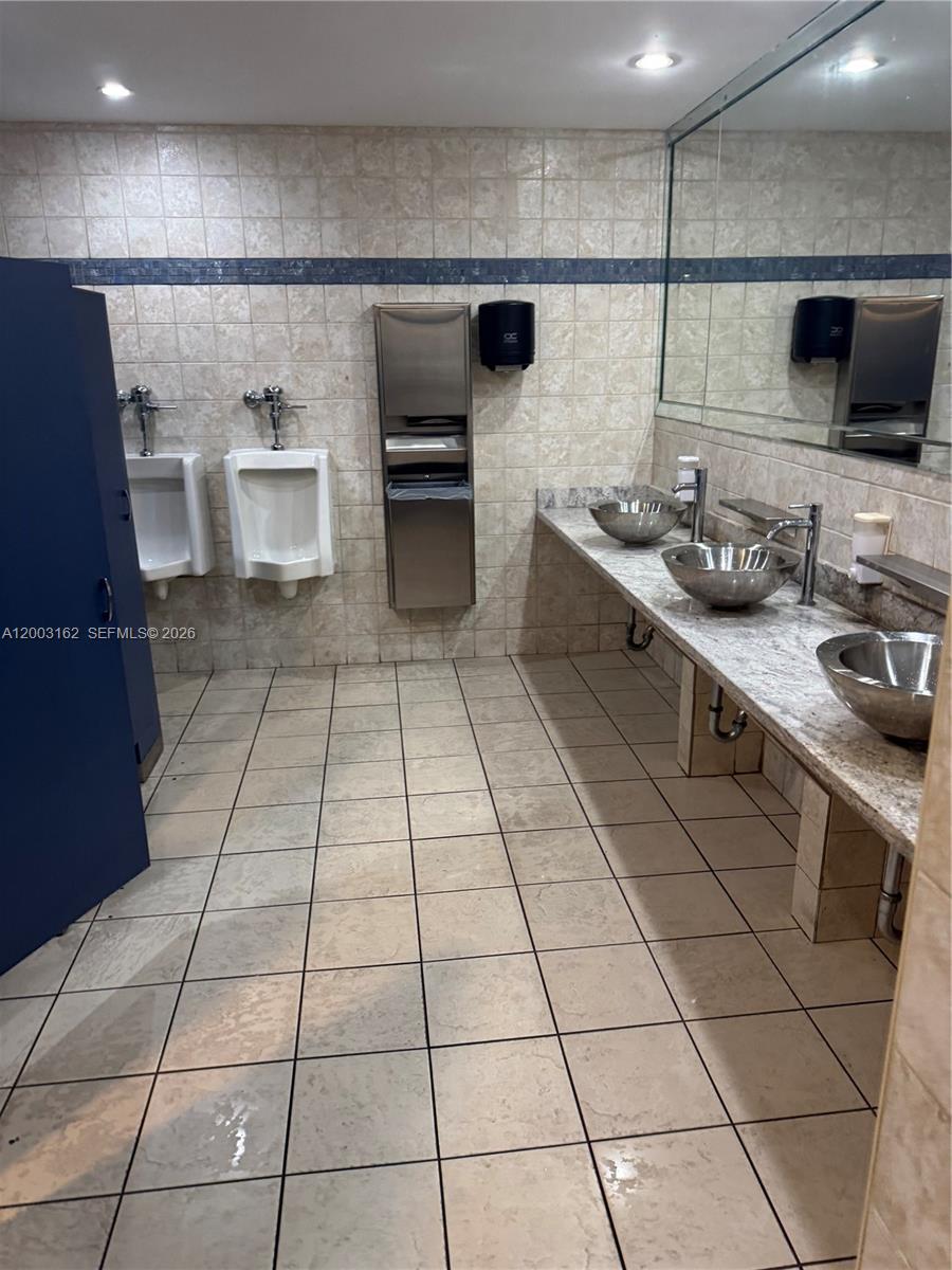 A public restroom features two urinals, three vessel sinks on a stone vanity, and tile flooring — 717 Ponce De Leon Blvd # 323, Coral Gables FL 33134, CORAL GABLES, FL