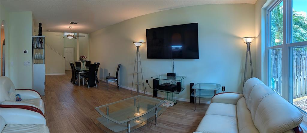 A living room with light wood-look flooring, a wall-mounted television, and a dining area beyond — 2983 COVEWOOD PLACE, CLEARWATER, FL
