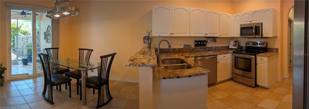 A kitchen with white cabinets and granite countertops opens to a dining area with patio access — 2983 COVEWOOD PLACE, CLEARWATER, FL