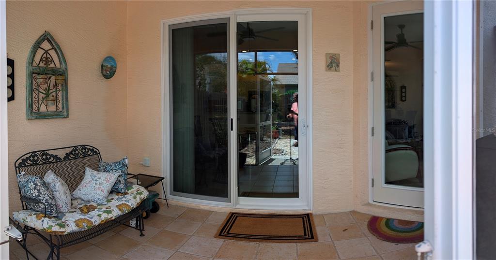 A covered patio features a metal bench, sliding glass doors, and a single glass door — 2983 COVEWOOD PLACE, CLEARWATER, FL