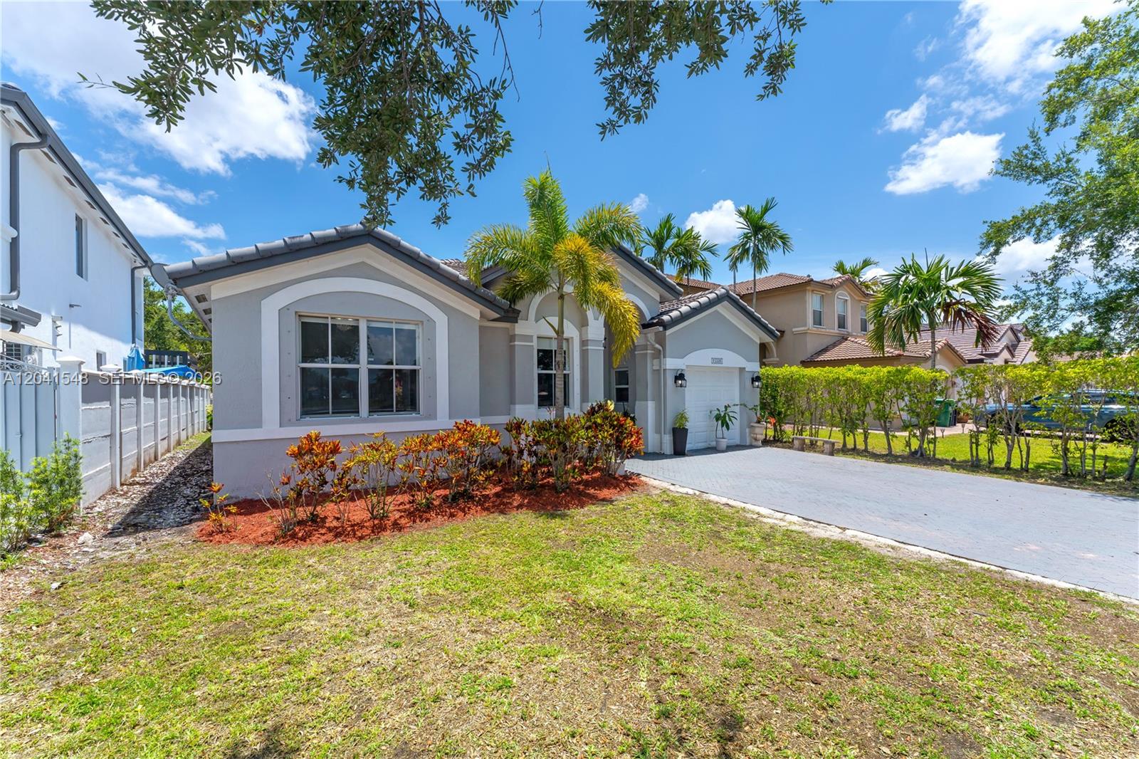 A single-story gray house features a paved driveway, a palm tree, and landscaped front bushes — 15506 SW 25th Ter, Miami FL 33185, MIAMI, FL