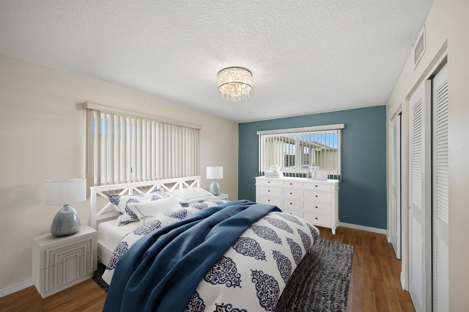 A bedroom features a blue accent wall, white furniture, a patterned bedspread, and wood flooring — 130 NE 26th Avenue # 4090, Boynton Beach FL 33435, BOYNTON BEACH, FL