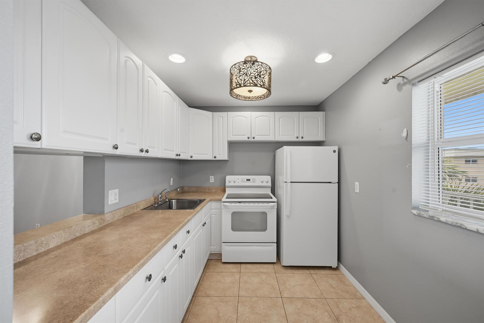 A kitchen features white cabinets, tan countertops, a white stove, and a white refrigerator — 130 NE 26th Avenue # 4090, Boynton Beach FL 33435, BOYNTON BEACH, FL