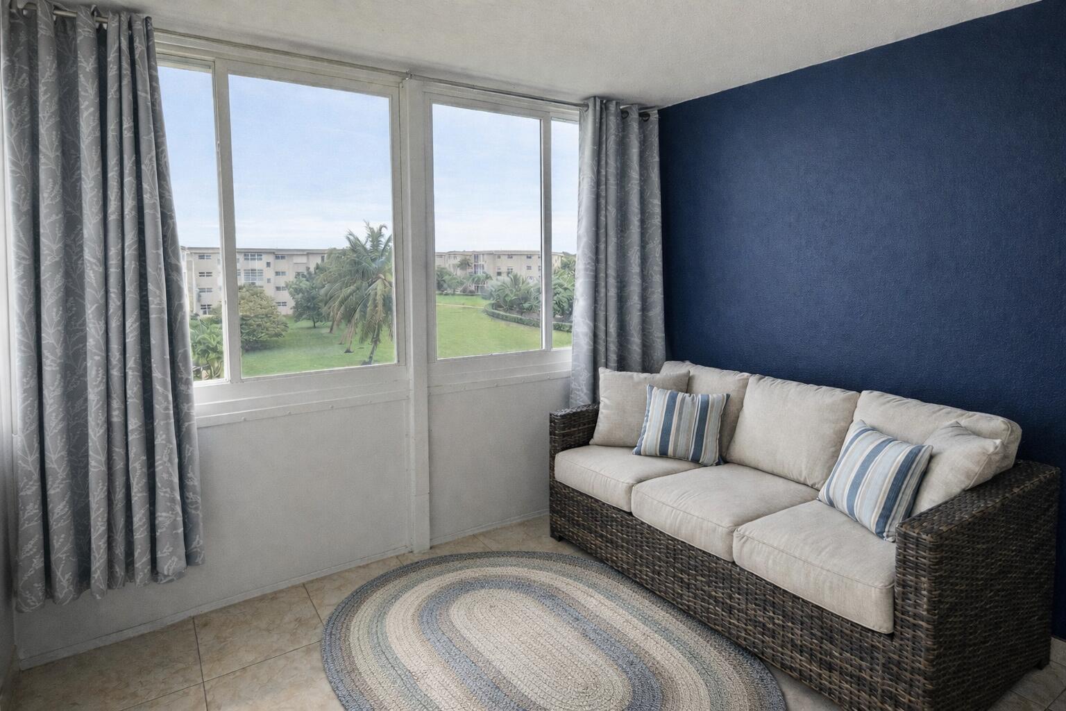 A sunroom features a wicker sofa, a blue accent wall, and large windows overlooking greenery — 130 NE 26th Avenue # 4090, Boynton Beach FL 33435, BOYNTON BEACH, FL