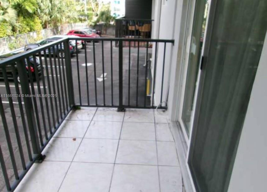 A balcony with white tile flooring and a black metal railing overlooks a parking lot — 900 SW 84th Ave # 207A, Miami FL 33144, MIAMI, FL