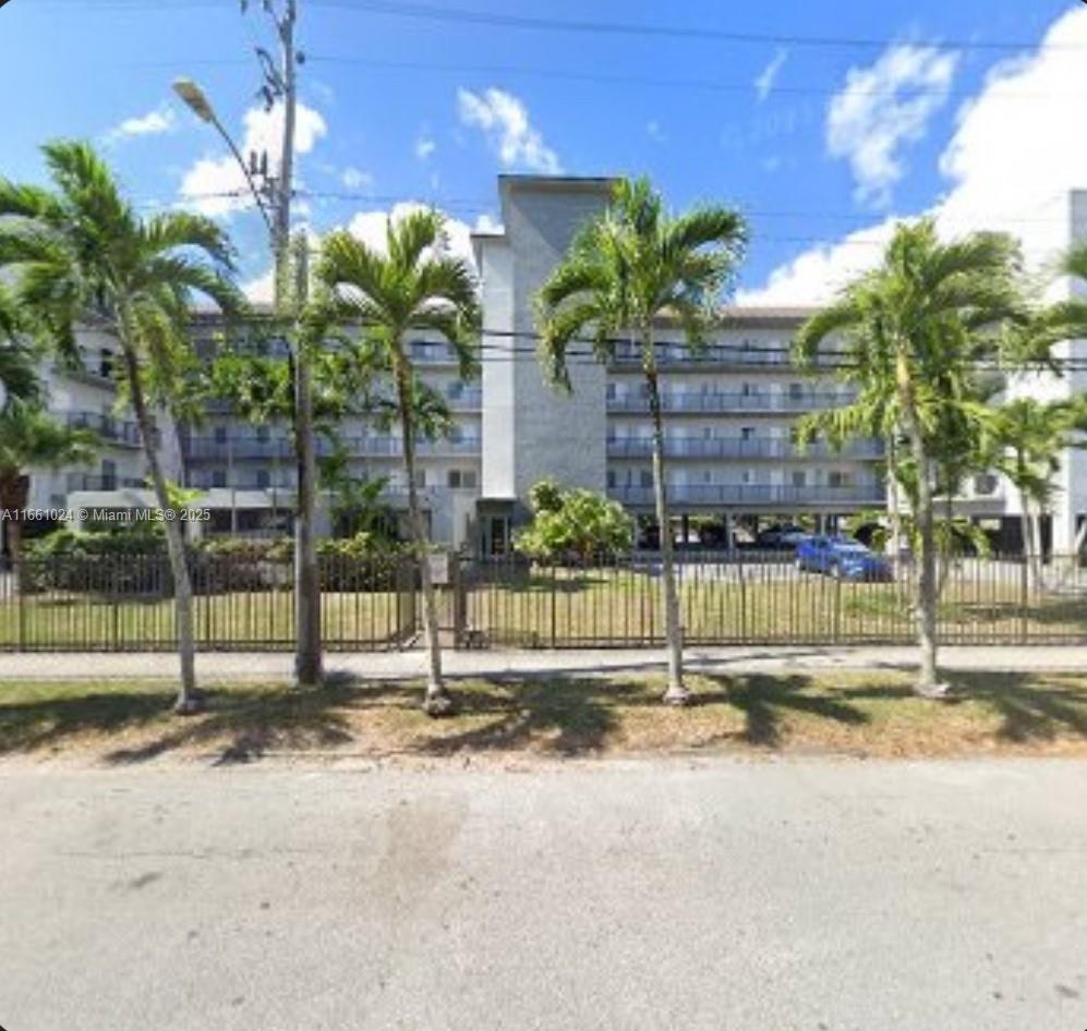A multi-story apartment building is viewed from the street behind a metal fence and palms — 900 SW 84th Ave # 207A, Miami FL 33144, MIAMI, FL