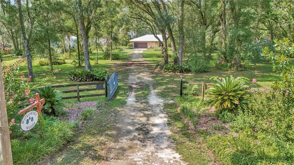 A dirt driveway leads through a gated entrance toward a house surrounded by trees — 17690 SE 66 PLACE, MORRISTON, FL