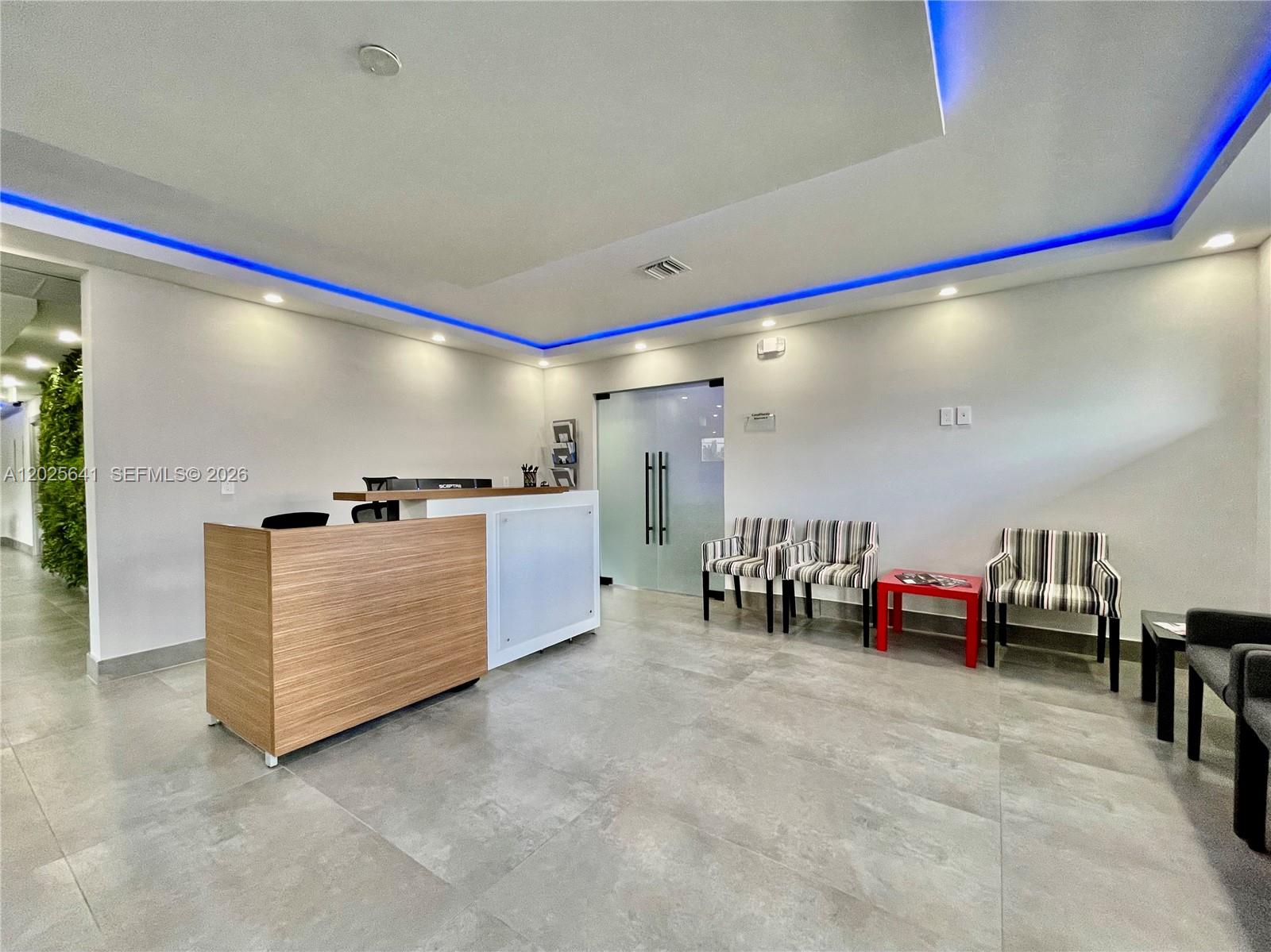 A modern office reception area features a wood-paneled desk, striped chairs, and blue ceiling lighting — 6280 W Atlantic Blvd, Margate FL 33063, MARGATE, FL
