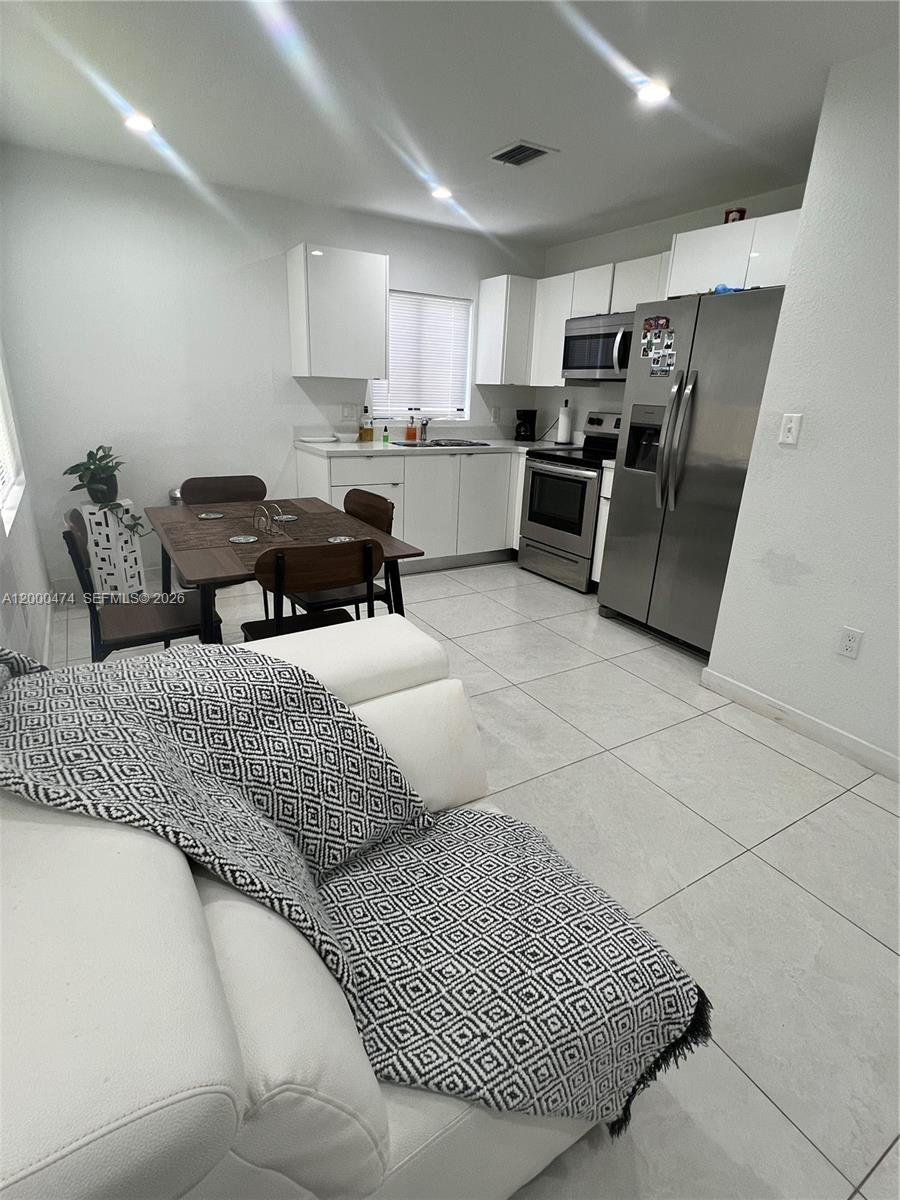 This kitchen features white cabinetry, stainless steel appliances, and a dining table with chairs — 2954 NW 57th St # 2954, Miami FL 33142, MIAMI, FL