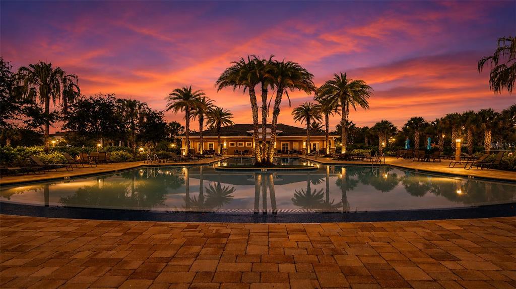 A swimming pool reflects palm trees and a building under a vibrant sunset sky — 12356 TRAILHEAD DRIVE, BRADENTON, FL