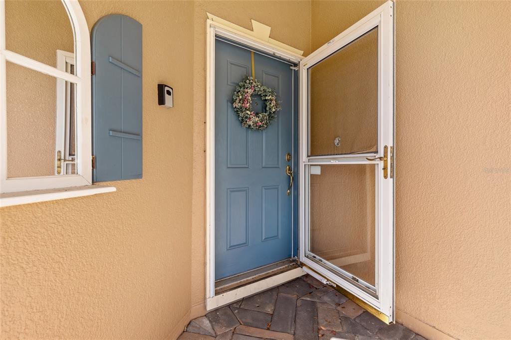 A blue front door with a wreath and a screen door on a paved porch — 632 PORTOFINO DRIVE, KISSIMMEE, FL