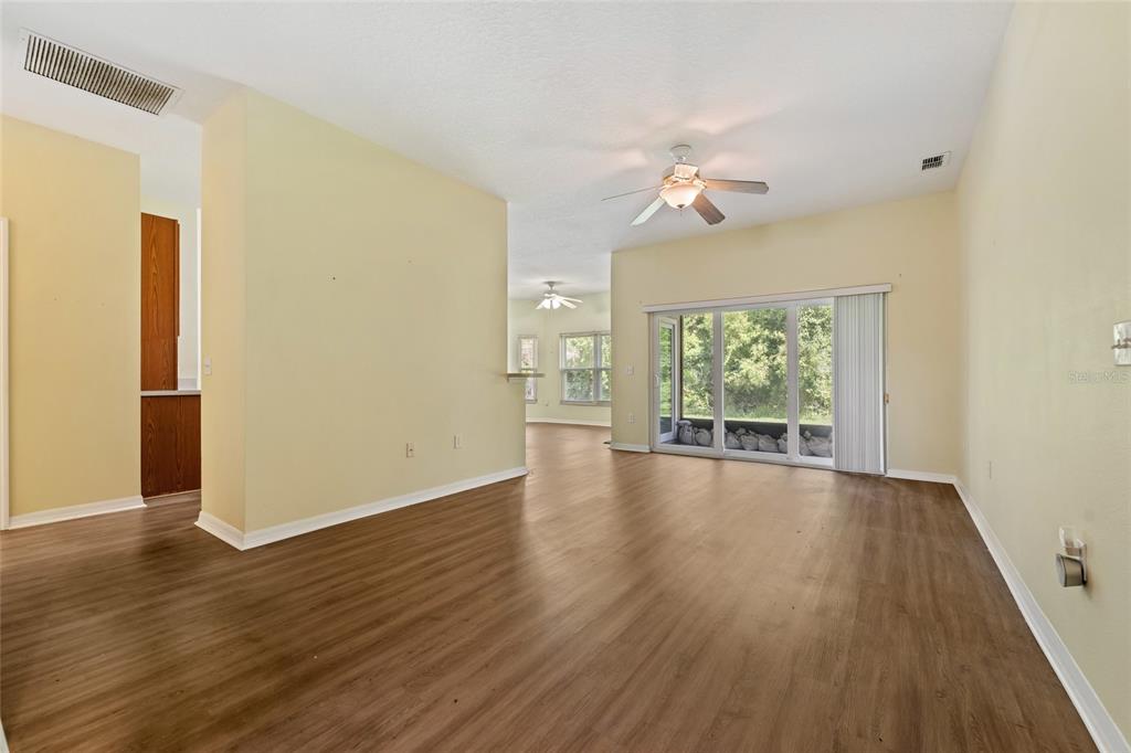 An empty living room with light-colored walls, wood-look flooring, a ceiling fan, and sliding glass doors — 632 PORTOFINO DRIVE, KISSIMMEE, FL