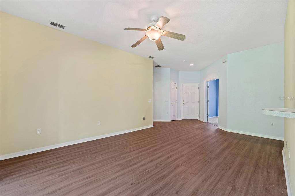 An empty living room with light-colored walls, wood-look flooring, and a ceiling fan — 632 PORTOFINO DRIVE, KISSIMMEE, FL