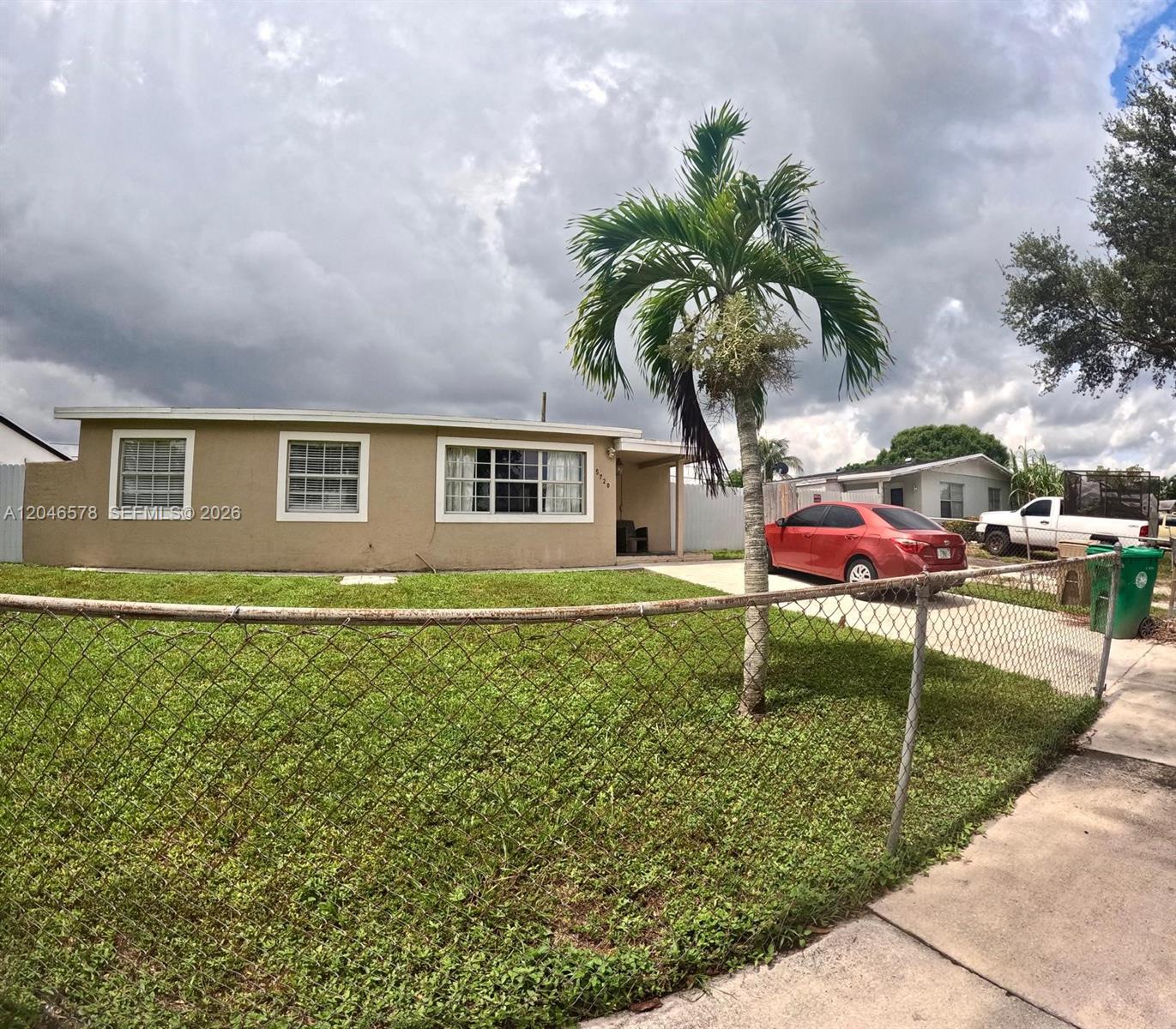 A single-story tan house features a chain-link fence, a palm tree, and a red car — 5720 SW 38th Ct # 5720, Davie FL 33314, DAVIE, FL