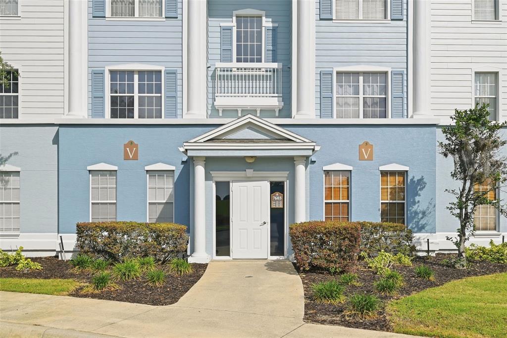 The exterior of a blue multi-story apartment building features a central entrance with columns — 7603 HERITAGE CROSSING WAY UNIT 102, REUNION, FL