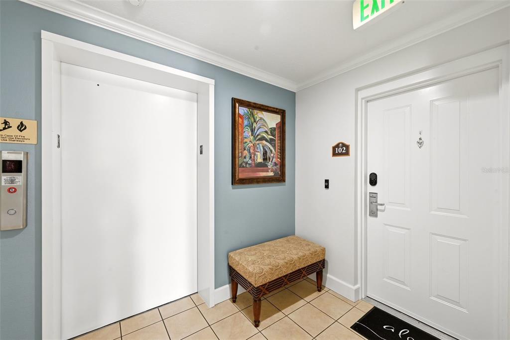 An indoor entryway features a white elevator, a framed painting, a bench, and a door — 7603 HERITAGE CROSSING WAY UNIT 102, REUNION, FL