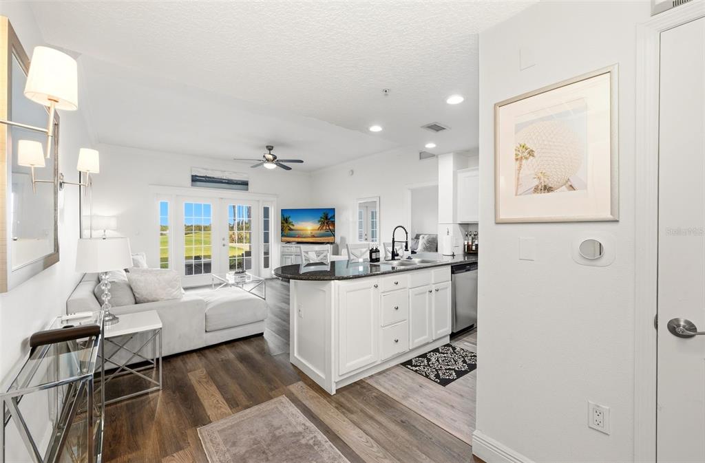 An open-concept living room and kitchen feature white cabinetry, dark countertops, and glass patio doors — 7603 HERITAGE CROSSING WAY UNIT 102, REUNION, FL