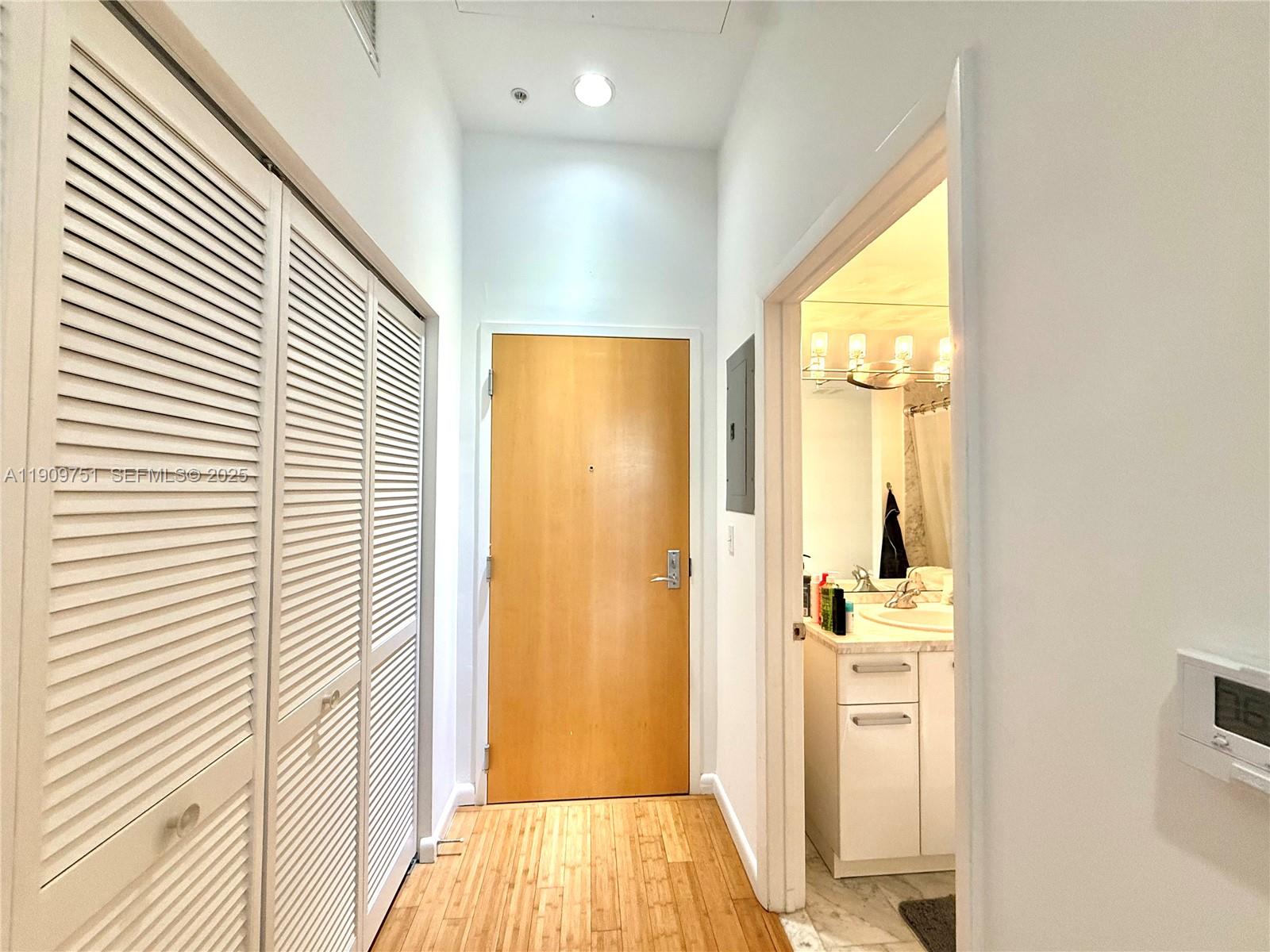 A hallway features light wood flooring, louvered closet doors, a wooden entrance door, and a bathroom — 253 NE 2nd St # 219, Miami FL 33132, MIAMI, FL