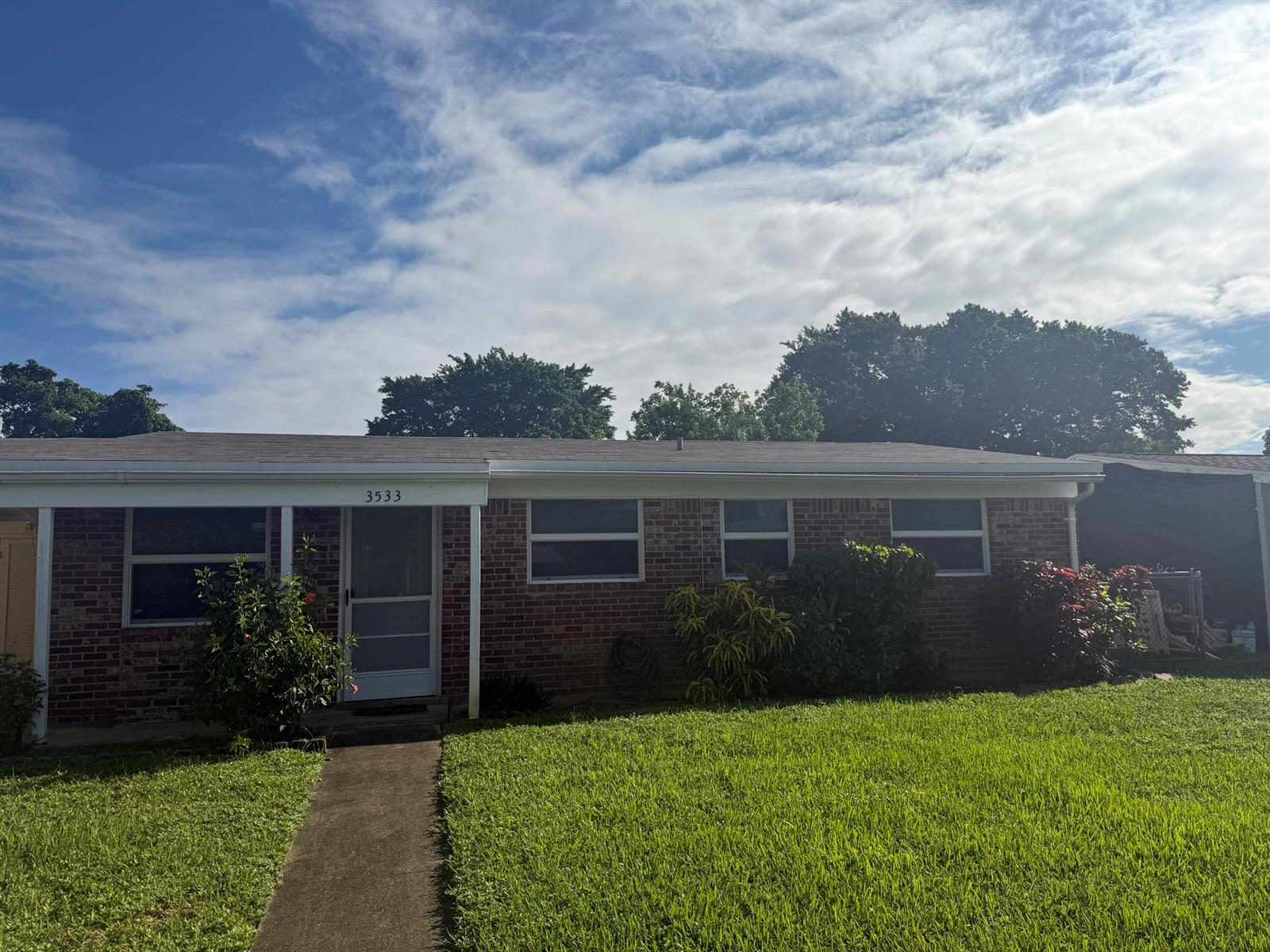 A single-story brick house with a front porch, walkway, and lawn under a cloudy sky — 3533 Florida Boulevard, Palm Beach Gardens FL 33410, PALM BEACH GARDENS, FL