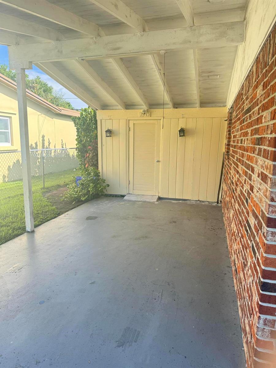 A covered patio features a concrete floor, a yellow door, and a brick wall — 3533 Florida Boulevard, Palm Beach Gardens FL 33410, PALM BEACH GARDENS, FL